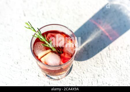 Blick von oben auf ein Glas mit rotem erfrischendem Sommergetränk oder Rotwein, Eiswürfel, Wassermelonen- und Rosmarinzweigen. Stockfoto
