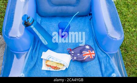Komposition in blauen Farbtönen eines Picknick auf dem Gras mit aufblasbarer Matratze, Wasserflasche, Sandwich, Glas mit Stroh und australische Flagge Stockfoto