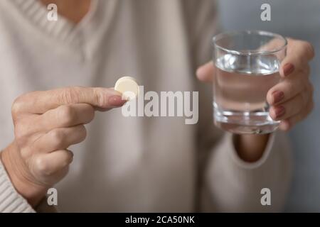 Ältere weibliche Hände halten Pille und Glas Wasser in der Nähe Stockfoto