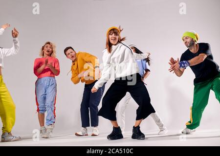 Junge Tänzerin in Bewegung, gekleidet in weißem Hoodie und breiten schwarzen Hosen, zeigt expressiven Tanz, Blick auf die Kamera mit fröhlichem Ausdruck, hav Stockfoto