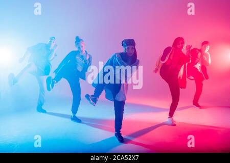 Junge moderne Tanzgruppe von sechs erwachsenen jungen Menschen üben Tanz auf bunten Hintergrund. Modisch gekleidete Jugendliche bewegen sich über verschwommene Disco Stockfoto