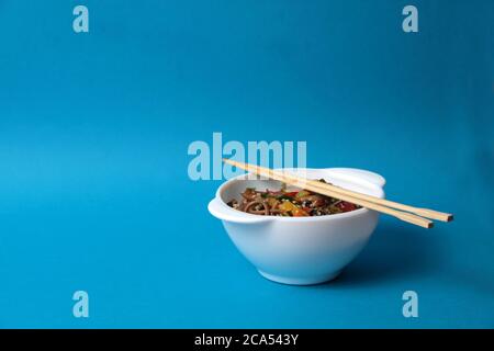 Eine Schüssel mit Wok-Nudeln und Essstäbchen isoliert auf blauem Hintergrund. Das Bild enthält den Kopierbereich Stockfoto