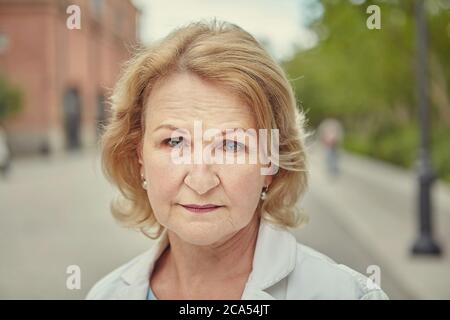 Ältere kaukasische Geschäftsfrau über 62 Jahre alt mit seriösen und selbstbewussten Blick steht im Freien am Tag. Sie hat blonde Haare und wrink Stockfoto