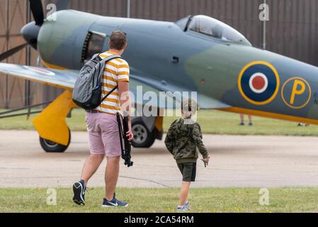 Imperial war Museum Duxford, Cambridgeshire, Großbritannien. August 2020. Nach einer langen Stilllegung durch die COVID-19 Coronavirus-Sperre öffnete das Museum am 1. August wieder seine Türen für Besucher. Heute hat das Museum seine erste Luftvorstellungsveranstaltung abgehalten – mit dem Titel A Showcase Day. Es war eine vorab gebuchte Ticket-only-Veranstaltung mit stark reduziertem Besucherlimit, und die Besucher mussten strenge Richtlinien einhalten, wenn sie die Innenausstattungen betraten. Vater und Sohn beobachten ein Jagdflugzeug des Hawker Fury aus dem zweiten Weltkrieg Stockfoto