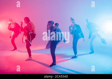 Gruppe von verschiedenen jungen Hip-Hop-Tänzern im Studio mit speziellen Lichteffekten in blauen und rosa Farben Stockfoto