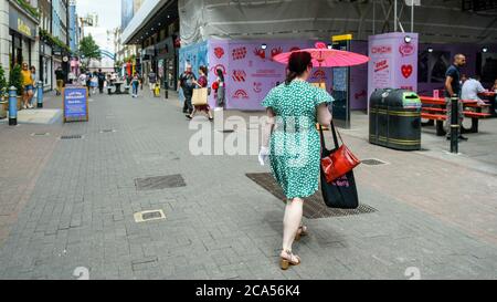 London, Großbritannien. August 2020. Eine Frau, die einen Sonnenschirm trägt, geht an Picknicktischen vorbei, die in der Carnaby Street aufgestellt wurden und Menschen mit Essen zum Mitnehmen einen Ort zum Essen bieten. Schilder auf den Tischen erinnern die Menschen daran, sich weiterhin sozial zu distanzieren, während die Coronavirus-Pandemie andauert. Kredit: Stephen Chung / Alamy Live Nachrichten Stockfoto