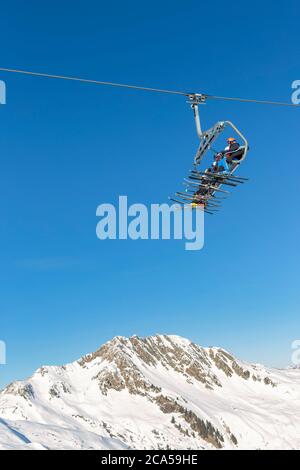 Skifahrer saßen an einem sonnigen Tag auf einem Sessellift mit einem klaren blauen Himmel und schneebedeckten Bergen im Hintergrund Stockfoto