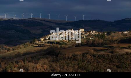 Frankreich, Aude (11), Limousin, Roquetaillade, Blick auf ein Dorf in einer bergigen Umgebung mit einem stürmischen Himmel mit Windturbinen im Hintergrund Stockfoto