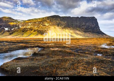 Isländische Landschaft durch zerbrochene Wolke, Moore können auf der Ebene, die bis zu den Felswänden gesehen werden. Stockfoto