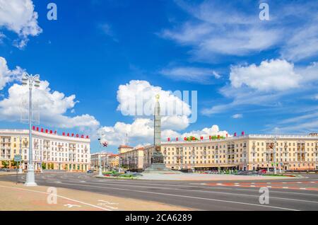 Der Siegesplatz in der Stadt Minsk mit dem Granitdenkmal des Sieges und den roten Buchstaben auf den Gebäuden lesen die Heldentat des Volkes ist unsterblich, der blaue Himmel weiß die Wolken am sonnigen Tag, die Republik Weißrussland Stockfoto