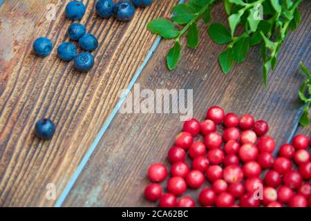 Waldbeeren auf dunklem rustikalem Holzhintergrund. Preiselbeeren und Heidelbeeren mit grünen Blättern auf altem Holztisch. Draufsicht Stockfoto