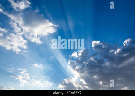 Sonnenstrahlen, die zwischen den Wolken in einem intensiven blauen Himmel ausstrahlen Stockfoto