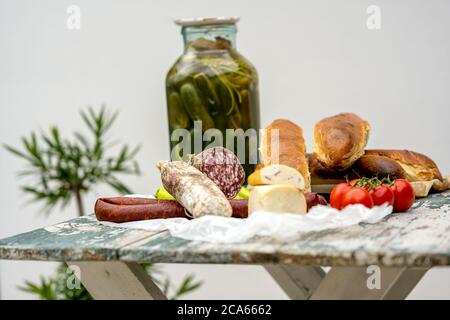 Stilvoller rustikaler Picknicktisch mit hausgemachten Salami, Wurst, Käse und Brot darauf, zusammen mit einigen frisch gepflückten Tomaten und grünen Paprika und Stockfoto