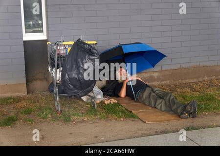 Obdachloser, der unter einem Sonnenschirm neben einer Straße in Vancouver, BC, Kanada schläft Stockfoto