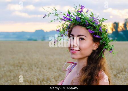 Glücklich lächelndes Mädchen mit langen Haaren mit einem Blumenkranz auf dem Kopf in Weizenfeld Stockfoto