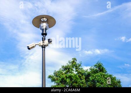 Zwei weiße Überwachungskameras an der Metalllampe im öffentlichen Park. Stockfoto