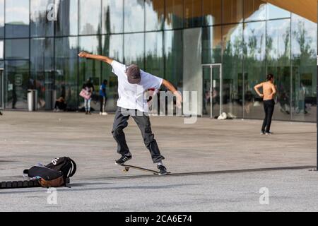 Junger Mann oder Teenager mitten in einem Skateboard-Trick vor der Central Library Oodi in Helsinki, Finnland Stockfoto