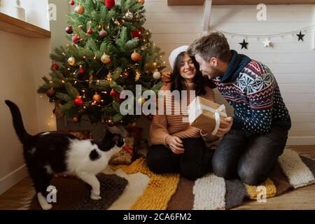Frohe Weihnachten. Glücklich aufgeregt Paar Austausch weihnachtsgeschenke unter weihnachtsbaum mit Lichtern. Junge Familie hält Überraschung präsent, glücklicher Moment Stockfoto