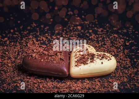 Zwei herzförmige Pralinen aus Milch und weißer Schokolade auf der Schiefertafel, mit geriebener Schokolade überzogen. Desserts zum Valentinstag. Stockfoto