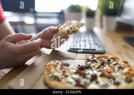 Mann, der Pizza am Arbeitsplatz vor dem Computer isst Stockfoto