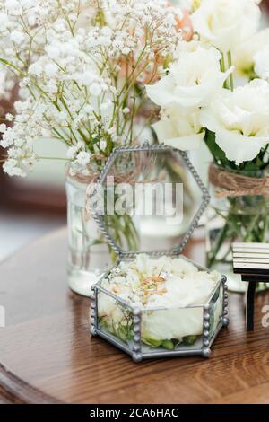 Goldene Eheringe mit Diamanten in der Box mit Rosen auf dem Hintergrund der weißen Blumen Stockfoto