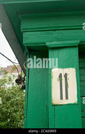 Hausnummer 11.ein altes Schild an der grünen Holzfassade des Hauses. Historische Gebäude. Stockfoto