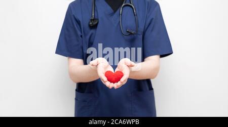 Der Arzt hält ein rot gestricktes Herz. Kardiologie. Coronavirus, covid-19, Gesundheitskonzept. Stockfoto