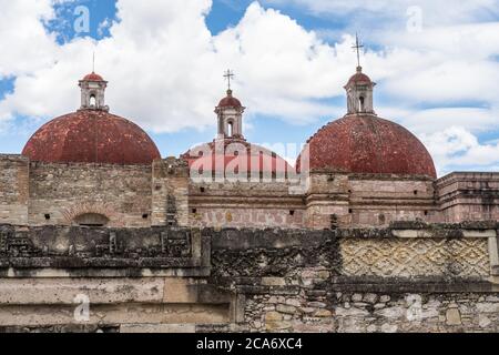 Steinmetzplatten an den Wänden des Hofes B (Viereck B), in den Ruinen der Zapotec-Stadt Mitla, in der Nähe von Oaxaca, Mexiko. Dahinter ist der dom Stockfoto