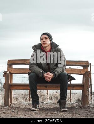 Junger Mann, der auf einer Bank sitzt und seine Hände zusammenhält Stockfoto