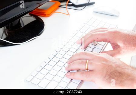 Männliche Hände, die auf einer grauen Computertastatur mit weißen Tasten tippen. Arbeit und Büro. Technologie und Kreativität. Weißer Hintergrund. Stockfoto