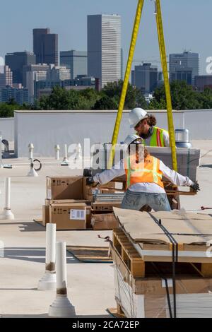 Denver, Colorado - Sonnenkollektoren und andere Geräte für eine Solaranlage werden an die Spitze eines neuen erschwinglichen Wohngebäudes gehoben. Das so Stockfoto