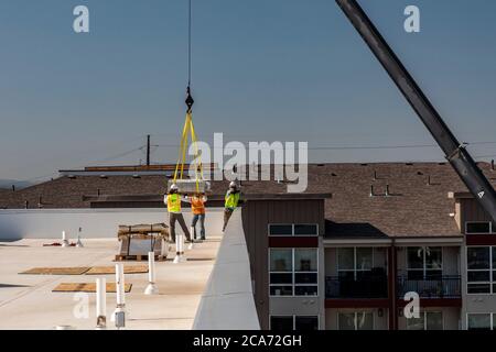 Denver, Colorado - Sonnenkollektoren und andere Geräte für eine Solaranlage werden an die Spitze eines neuen erschwinglichen Wohngebäudes gehoben. Das so Stockfoto