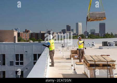 Denver, Colorado - Sonnenkollektoren und andere Geräte für eine Solaranlage werden an die Spitze eines neuen erschwinglichen Wohngebäudes gehoben. Das so Stockfoto