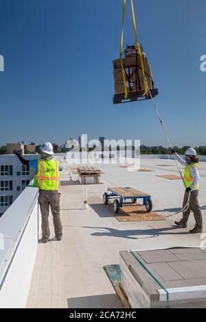 Denver, Colorado - Sonnenkollektoren und andere Geräte für eine Solaranlage werden an die Spitze eines neuen erschwinglichen Wohngebäudes gehoben. Das so Stockfoto