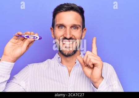 Junger schöner Mann Controlling Temperatur halten Thermometer über lila Hintergrund lächelnd glücklich zeigt mit Hand und Finger zur Seite Stockfoto