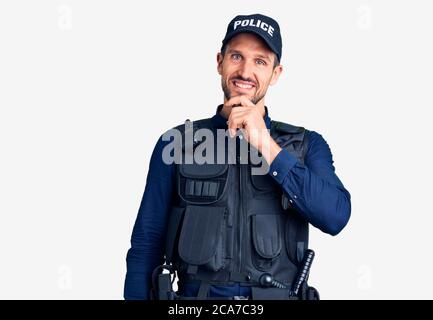 Junger gutaussehender Mann in Polizeiuniform, der selbstbewusst auf die Kamera schaut, lächelt mit gekreuzten Armen und erhobener Hand am Kinn. Positiv denken. Stockfoto