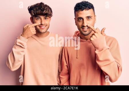 Junge Homosexuell Paar tragen lässige Kleidung zeigt mit der Hand Finger auf Gesicht und Nase, lächelnd fröhlich. Beauty-Konzept Stockfoto