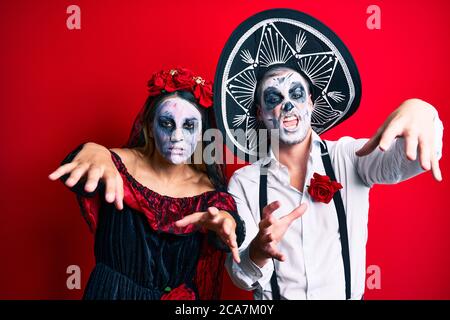 Schönes Paar trägt Tag der Toten Kostüm gestikuliert als Zombie über isolierten roten Hintergrund. Stockfoto