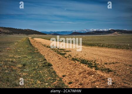 Unbefestigte Straße, die in die Ferne führt. Berge sichtbar in der Entfernung von Colorado Flugzeug. Große schneebedeckte Berge hinter staubigen Trail Stockfoto