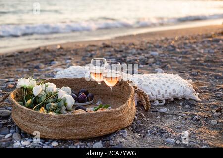 Horizontales Bild des Strandpicknicks mit Wein, Feigen, Croissants und Lisianthus Blumen in einem gewebten Korb. Negatives Leerzeichen. Stockfoto