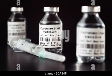 Coronavirus Covid-19 Impfstoffkonzept - drei Glasfläschchen auf schwarzem Tisch, hypodermische Spritzennadel in der Nähe, Nahaufnahme Detail (Label eigenes Design - Dummy dat Stockfoto