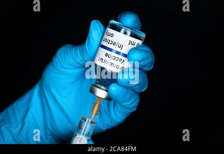Hand in blauen Handschuhen mit hypodermischer Spritze und Coronavirus-Impfstoff (Aufkleber eigenes Design, nicht echtes Produkt), Injektion es Nahaufnahme Detail, schwarze Rückseite Stockfoto