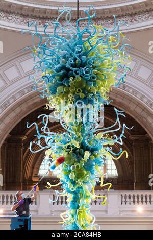 Museumstechniker Andy Monk reinigt den 27 Meter langen Rotunda-Kronleuchter von Dale Chihuly, der aus 1,300 blauen und grünen Glaselementen besteht, im Victoria and Albert Museum in London, während er sich auf die Wiedereröffnung am 6. August vorbereitet. Stockfoto