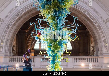 Museumstechniker Andy Monk reinigt den 27 Meter langen Rotunda-Kronleuchter von Dale Chihuly, der aus 1,300 blauen und grünen Glaselementen besteht, im Victoria and Albert Museum in London, während er sich auf die Wiedereröffnung am 6. August vorbereitet. Stockfoto