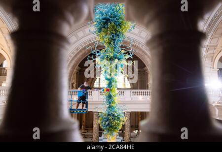 Museumstechniker Andy Monk reinigt den 27 Meter langen Rotunda-Kronleuchter von Dale Chihuly, der aus 1,300 blauen und grünen Glaselementen besteht, im Victoria and Albert Museum in London, während er sich auf die Wiedereröffnung am 6. August vorbereitet. Stockfoto