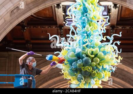 Museumstechniker Andy Monk reinigt den 27 Meter langen Rotunda-Kronleuchter von Dale Chihuly, der aus 1,300 blauen und grünen Glaselementen besteht, im Victoria and Albert Museum in London, während er sich auf die Wiedereröffnung am 6. August vorbereitet. Stockfoto