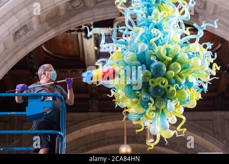 Museumstechniker Andy Monk reinigt den 27 Meter langen Rotunda-Kronleuchter von Dale Chihuly, der aus 1,300 blauen und grünen Glaselementen besteht, im Victoria and Albert Museum in London, während er sich auf die Wiedereröffnung am 6. August vorbereitet. Stockfoto