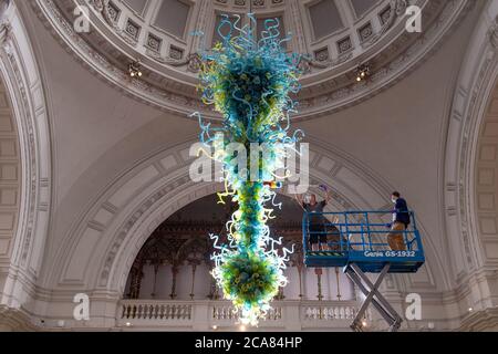 Museumstechniker Andy Monk reinigt den 27 Meter langen Rotunda-Kronleuchter von Dale Chihuly, der aus 1,300 blauen und grünen Glaselementen besteht, im Victoria and Albert Museum in London, während er sich auf die Wiedereröffnung am 6. August vorbereitet. Stockfoto