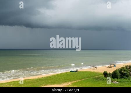 Strand vor Sturm. Negombo, Sri Lanka. Wolkiger und dramatischer Himmel. Sonnenlicht am Strand mit Booten und Hütte Stockfoto