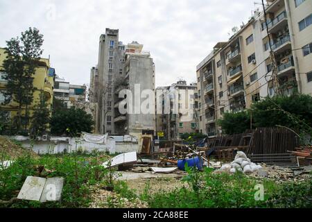 Gebäude während des Bürgerkriegs in Beirut beschädigt, umgeben von neuen Wohngebäuden, mit Schrott und Schrott auf dem Gras vor den Gebäuden. Stockfoto